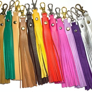 Puede incluir: Surtido de 12 llaveros de borla de cuero en varios colores, incluyendo blanco, marrón, verde, beige, marrón, amarillo, naranja, rosa, lavanda, morado, plateado. Cada llavero tiene un anillo de metal y un pequeño botón.