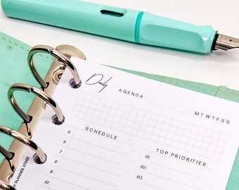 May include: A white daily planner with a green cover. The planner has a schedule section, a top priorities section, a notes section, and a checklist section. The planner is open to the daily page, which has a grid for scheduling and a space for notes.