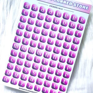 Può includere: Un foglio di adesivi con un design rosa e viola. Ogni adesivo presenta una lettera dell'alfabeto in bianco su uno sfondo quadrato. Il foglio è etichettato "MY FAIRY PLANNER STORE" e "STICKERS.110.12".