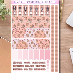 Può includere: Un foglio di adesivi intitolato MY FAIRY PLANNER STORE con motivi a quadri rosa e marroni, intestazioni giornaliere da MON a SUN e illustrazioni di piccole creature marroni. Include etichette rosa a forma di bandiera e testo per le attività.