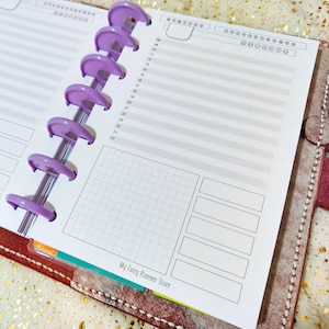 Könnte beinhalten: Ein lilafarbener Planer mit einem karierten Abschnitt und leeren Zeilen zum Schreiben. Der Planer hat eine lilafarbene Bindung und der Text "My Fairy Planner Store" ist unten aufgedruckt.