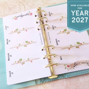 Può includere: Un'agenda aperta su una pagina di agosto, con un raccoglitore dorato. La pagina ha un design floreale e la parola "Agosto" in alto. Il testo "NOW AVAILABLE FOR YEAR 2027" è in uno striscione turchese. L'agenda è in una custodia azzurra.