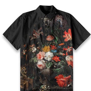 Puede incluir: Una camisa negra de manga corta con botones y estampado floral. El estampado presenta una variedad de flores en tonos rojos, rosas, blancos y amarillos, dispuestas en un jarrón. Las flores están rodeadas de hojas y enredaderas verdes. La camisa tiene un cuello abotonado y un cierre de botones.