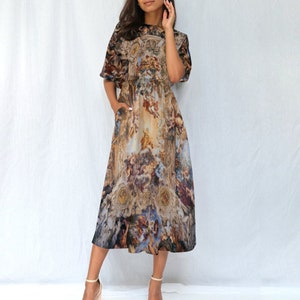 Peut inclure: Une robe mi-longue à imprimé de peinture de style Renaissance en brun, bleu et or. La robe a un col rond, des manches courtes et un corsage ajusté.