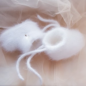 May include: White fuzzy baby booties with white laces. The booties are made of a soft, fluffy material and have a delicate, feminine look.