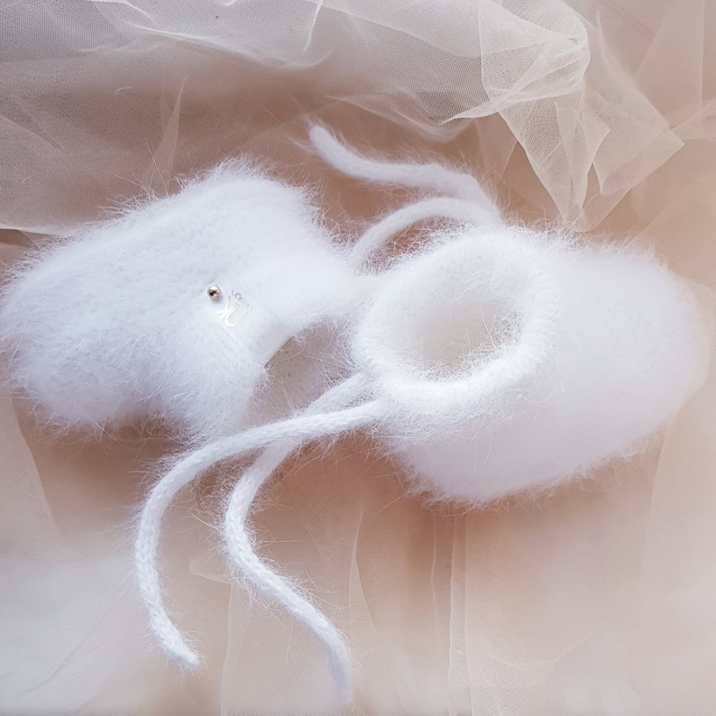 May include: White fuzzy baby booties with white laces. The booties are made of a soft, fluffy material and have a delicate, feminine look.