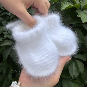 May include: A pair of white fuzzy baby booties made of knitted yarn.