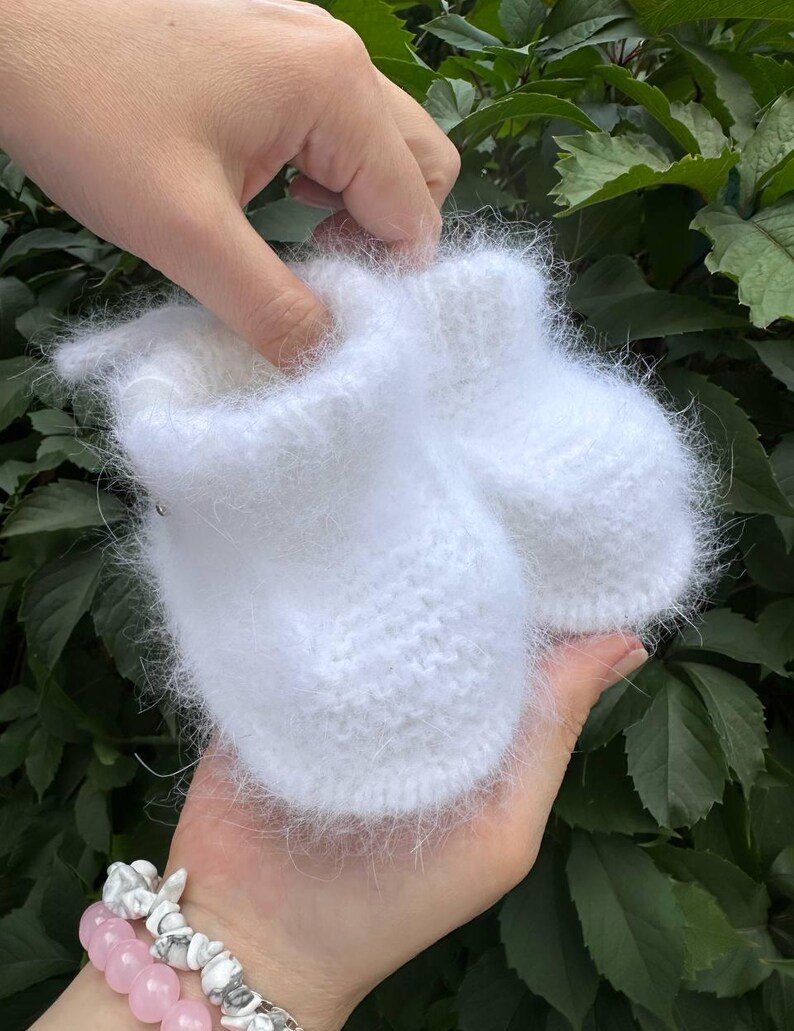 May include: A pair of white fuzzy baby booties made of knitted yarn.