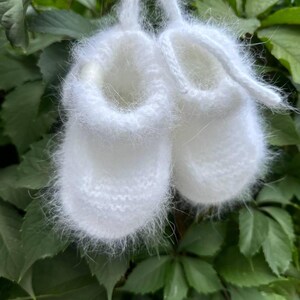 May include: A pair of white fuzzy baby booties with a white ribbon tie.