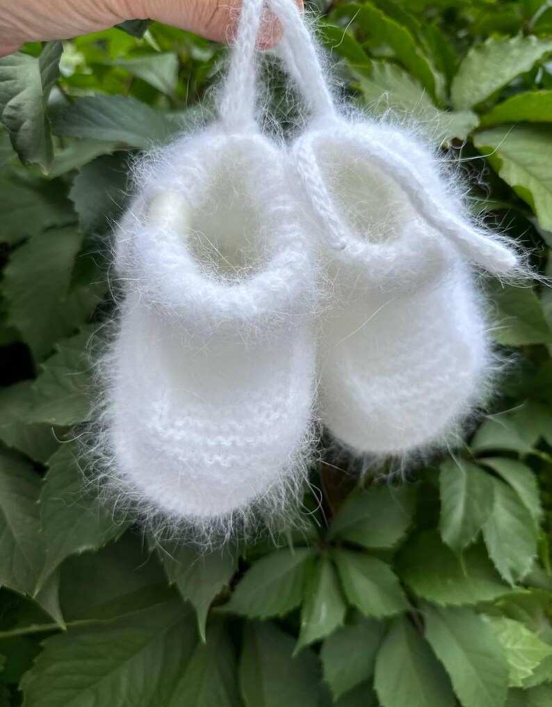 May include: A pair of white fuzzy baby booties with a white ribbon tie.