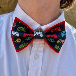 May include: A red bow tie with a black background and a pattern of colorful video game controllers.