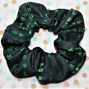 Może przedstawiać: Czarna scrunchie z nadrukowanym zielonym tekstem. Tekst to seria liter i cyfr, przypominająca kod komputerowy.