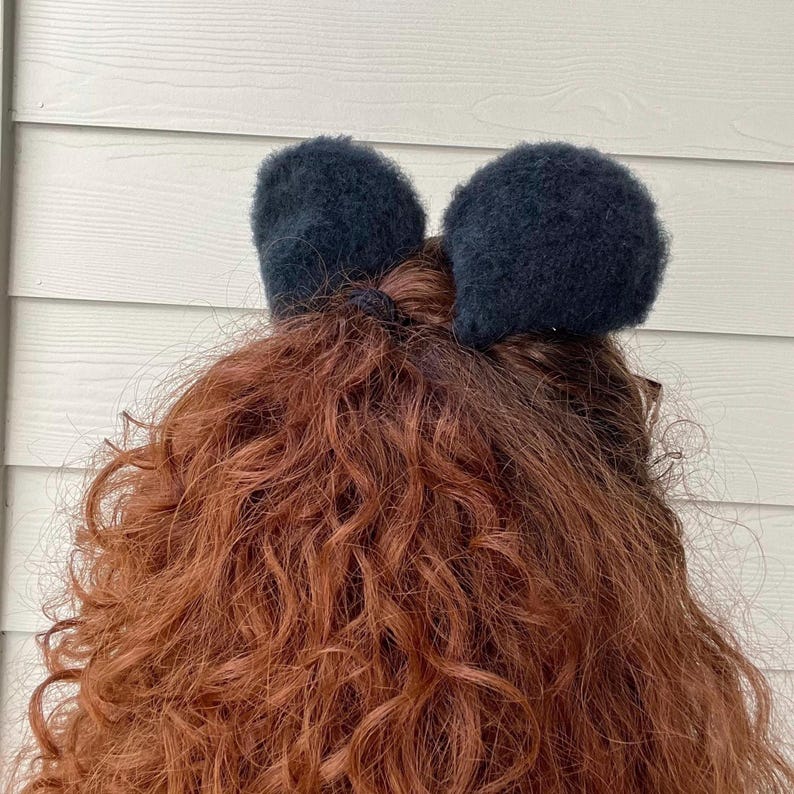 Pu&ograve; includere: Un fiocco per capelli nero e peloso con due grandi anelli. Il fiocco &egrave; indossato nei capelli di una persona.