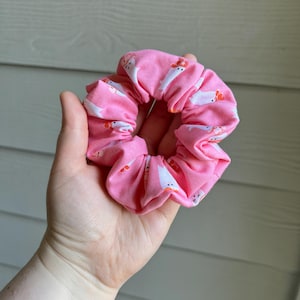 Op de afbeelding: Een roze stoffen scrunchie met een wit spookpatroon.