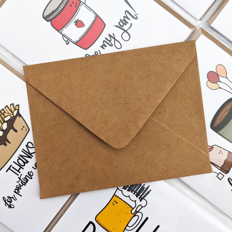 Peut inclure: Une enveloppe en papier kraft avec un rabat blanc. L'enveloppe est pos&eacute;e sur plusieurs cartes de v&oelig;ux avec diff&eacute;rentes illustrations.
