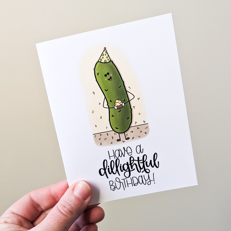 Cute pickle illustration holding a cupcake wearing a party hat saying have a dillightful birthday