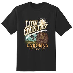 Puede incluir: Camiseta negra con un dise&ntilde;o gr&aacute;fico que presenta el texto "Low Country - A Way of Life" con un perro y una mecedora. El texto "North Carolina" tambi&eacute;n est&aacute; incluido en el dise&ntilde;o.