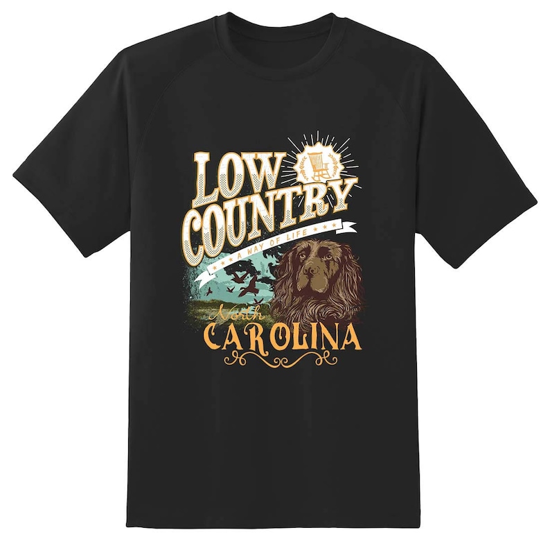 Puede incluir: Camiseta negra con un dise&ntilde;o gr&aacute;fico que presenta el texto "Low Country - A Way of Life" con un perro y una mecedora. El texto "North Carolina" tambi&eacute;n est&aacute; incluido en el dise&ntilde;o.