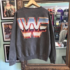 Può includere: Una felpa grigio antracite a maniche lunghe con un grande logo ricamato testurizzato e multicolore sul retro che riporta la scritta WWF. Le lettere sono progettate con un effetto sfumato che passa dal blu e bianco all'arancione e rosso.
