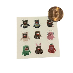 Könnte beinhalten: Ein Bogen mit neun bunten Monsteraufklebern mit verschiedenen Designs, darunter ein Panda, eine Fledermaus und eine Erdbeere. Eine Münze dient als Größenreferenz. Die Aufkleber befinden sich auf weißem Hintergrund.