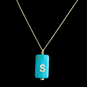 May include: A gold chain necklace with a turquoise pendant featuring the letter "S" in diamonds.