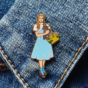 May include: A blue and white gingham dress with a red bow and a black cat in a yellow basket. The figure is wearing blue socks and red shoes.