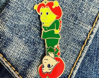 May include: A green and yellow enamel pin featuring a cartoon princess with red hair and a crown. The princess is upside down with her legs in the air.