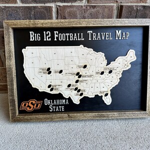May include: A framed wooden map of the United States with black footballs marking locations. The map is titled "Big 12 Football Travel Map" and features the Oklahoma State University logo with the text "Oklahoma State".