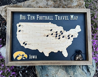 May include: A wooden framed map of the United States with a black background. The map is labeled "Big Ten Football Travel Map" and has a cutout of the United States with black footballs marking locations. The map also features a yellow and black Iowa Hawkeyes logo.
