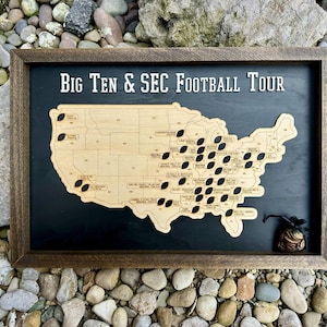 May include: Wooden framed map of the United States with a black background. The map is made of light-colored wood and features football-shaped cutouts. The text "Big Ten & SEC Football Tour" is at the top. A small bag of coins is in the bottom right corner.