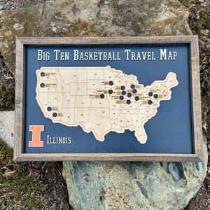 May include: A wooden map of the United States with a blue background and a wooden frame. The map shows the locations of Big Ten basketball teams. The text "Big Ten Basketball Travel Map" is at the top of the map. The text "Illinois" is at the bottom of the map.