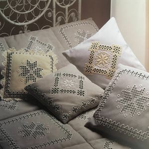 Peut inclure: Une tête de lit en osier blanc avec une couvre-lit et des oreillers brodés gris et blancs. Les oreillers ont un fond blanc avec un motif brodé gris.