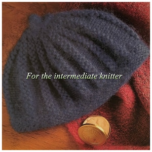 May include: A dark blue knitted beret, with a textured surface, resting on a red and brown fabric. The text "For the intermediate knitter" is visible on the beret.