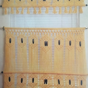 Puede incluir: Un juego de dos cenefas de macramé para ventanas con flecos y cuentas de madera. Las cenefas están hechas con hilo beige claro y tienen un diseño geométrico sencillo.