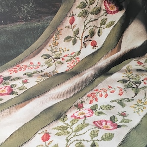 Puede incluir: Una manta de tiro de rayas blancas y verdes con un diseño floral que presenta rosas rosas, hojas verdes y bayas rojas. La manta está doblada y drapeada sobre una silla.