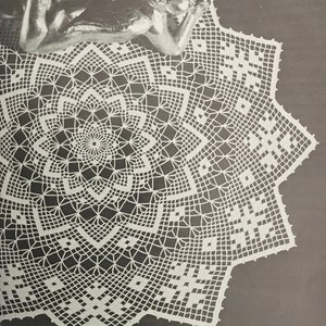 Puede incluir: Un encaje de ganchillo blanco con un diseño de estrella. El encaje está colocado sobre una superficie gris oscuro.