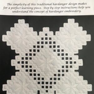 May include: White hardanger embroidery doily with a geometric pattern. The doily is a square with a star-shaped design in the center. The text "The Ultimate Teaching Doily**Plain and Simple**" is at the top of the image.