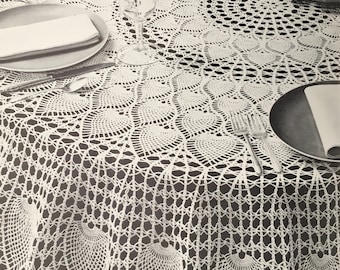Puede incluir: Un mantel redondo blanco tejido a ganchillo con un diseño calado detallado. El mantel está sobre una mesa puesta para una comida, con platos, cubiertos y vasos visibles. El intrincado patrón añade un toque de elegancia.