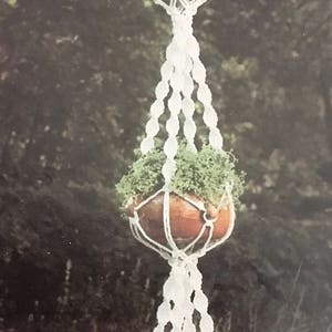 May include: Three hanging plant pots with green plants in them. The pots are brown and the macrame plant hangers are white.