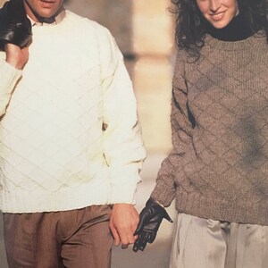 May include: Two people wearing sweaters with a diamond pattern. The person on the left is wearing a white sweater and the person on the right is wearing a brown sweater.