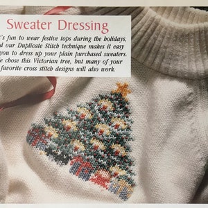 May include: A white sweater with a cross-stitch design of a Christmas tree with presents at the bottom. The text "Sweater Dressing" is at the top of the image. "It's fun to wear festive tops during the holidays, and our Duplicate Stitch technique makes it easy for you to dress up your plain purchased sweaters. We chose this Victorian tree, but many of your favorite cross stitch designs will also work." is written below the title.