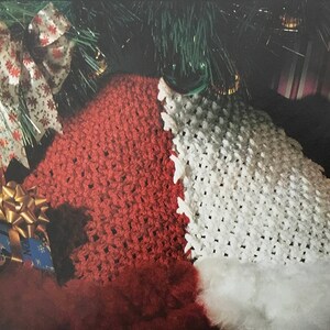 May include: A white crocheted Christmas stocking with a red crocheted cuff, surrounded by wrapped presents and a green Christmas tree.