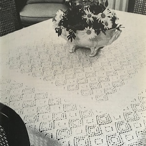 May include: A white crocheted tablecloth with a geometric pattern, featuring a white ceramic bowl filled with white daisies.