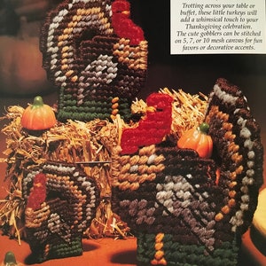 May include: Two brown and white felt turkeys with red heads and orange beaks. The turkeys are sitting on a bed of straw with small orange pumpkins. The text "Turkey Time" is printed in black on a white background.