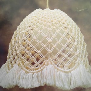 May include: A white crocheted lampshade with a fringe trim. The lampshade is made of a delicate, open-weave pattern.