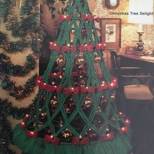 以下が含まれることがあります： 赤いリボンと金のオーナメントで飾られた緑色のマクラメ製のクリスマスツリー。ツリーは白いライトで飾られており、緑色のチュールスカートが付いています。画像には「Christmas Tree Delight」というテキストが表示されています。