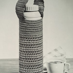 May include: A crocheted thermal bottle holder with a handle. The holder is made of a beige yarn and has a grid pattern. The bottle is white and has a lid.