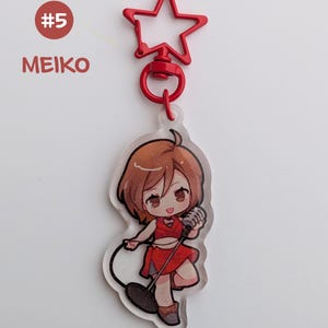 May include: A clear acrylic keychain featuring a cartoon character in a red outfit holding a microphone. The keychain has a red star-shaped clasp and the text "MEIKO" and "#5" in the upper left corner.