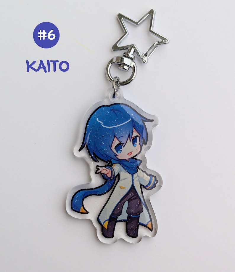 May include: A clear acrylic keychain featuring a blue-haired anime character with a white coat and blue scarf. The keychain has a silver star-shaped clasp and a ring. The text "#6 KAITO" is in a blue circle.