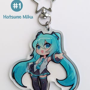 May include: A clear acrylic charm featuring a cartoon character with long, turquoise hair and a matching outfit. The charm is attached to a silver-colored star-shaped keychain. The text "#1 Hatsune Miku" is printed on the top left.